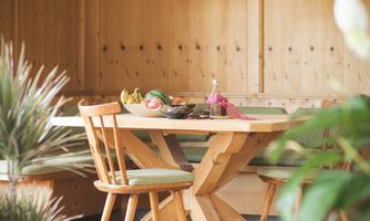 An inviting wooden dining table with two chairs, surrounded by green plants. Above the table hangs a decorative lamp in gentle colors.