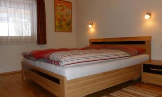 A cozy bedroom with a large bed and wooden floor. The room has large windows and modern decor.