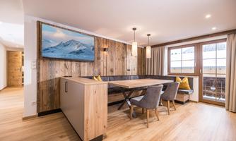 A modern living room with wood paneling and a large window. A dining area with comfortable chairs and a beautiful painting on the wall.