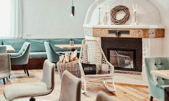 A cozy café with bright walls and modern furniture. The centerpiece is a fireplace, surrounded by a relaxed seating area.