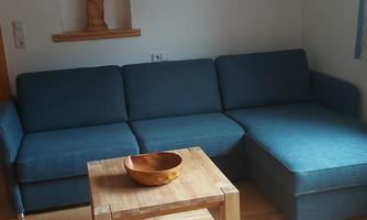 A cozy living room with a blue couch and a wooden table. Some decorative elements are hanging on the wall.