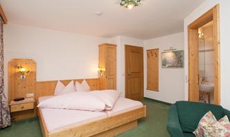 A cozy hotel room with a double bed and wooden paneling. A green couch and a view of the bathroom complement the space.