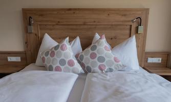 A cozy bed with white blankets and colorful pillows. The wooden cladding conveys a warm, inviting atmosphere.