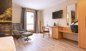 A modern hotel room with a cozy armchair and a desk. Large windows provide plenty of daylight.