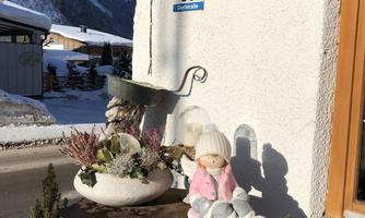 A cozy scene with a doll in a pink outfit on a table. In the background, snow-covered mountains and a wintry landscape can be seen.