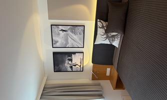 A modern bedroom with a large bed and elegant bedding. Two black-and-white photographs of snowy landscapes hang on the wall.