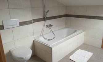 A modern bathroom with a bathtub and a shower. The walls are brightly tiled and there is a towel on the floor.