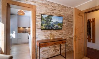 An inviting room with a wooden tray and a modern wall design made of stones. In the background, a kitchen and a beautiful landscape painting on the wall can be seen.