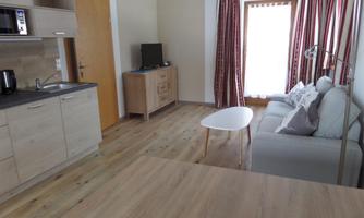 A modern living room with a kitchenette, a sofa, and a small table. Large windows provide plenty of natural light.