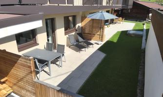 A cozy outdoor area with modern furniture and a sun umbrella. The space features a well-maintained lawn and a sunny terrace.