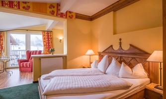 A cozy bedroom with a large double bed and wood decor. Adjacent to it, there is a seating area overlooking a balcony.