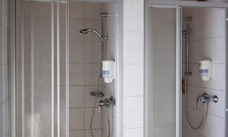 Two shower areas with clear glass partitions. Each area is equipped with a shower fixture and soap dispenser.