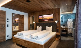 A modern bedroom with a double bed and wooden paneling. A picture of a sunset hangs on the wall, and two lamps stand next to the bed.