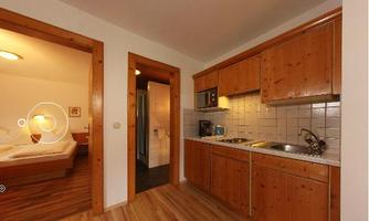 A cozy kitchen with wooden furniture and modern appliances. In the background, access to a bedroom is visible.