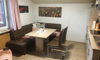 A cozy dining area with a table and a bench in warm tones. The walls are decorated with pictures of kitchen utensils.