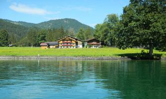 A tranquil lake with clear water and green shores. In the background, charming mountains and beautiful houses can be seen.
