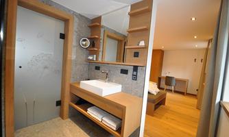 A modern bathroom with wooden shelves and an elegant sink. In the background, a cozy sleeping area is visible.