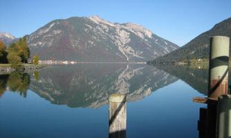A tranquil lake landscape with clear water and majestic mountains in the background. The reflection of the mountains in the water creates a peaceful atmosphere.