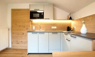A modern kitchen with bright wood and gray tones. It is well-equipped with a refrigerator, microwave, and an elegant vase.