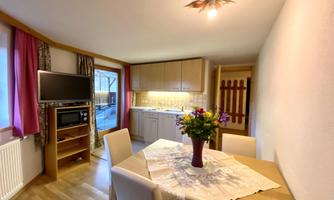 A cozy kitchen with a dining table and chairs. There is a television and a bouquet of flowers on the table.