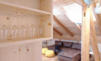 A well-furnished room with a shelf displaying glasses. In the background, a cozy sofa and a bright atmosphere are visible.