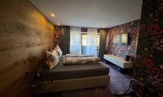 A modern bedroom with a colorful floral pattern on the walls. There is a large bed and a television, as well as plenty of daylight coming through the windows.