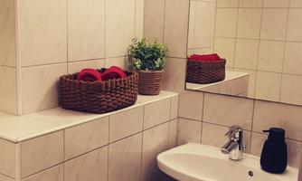 A modern bathroom with white tiles and a sink. On the shelf are towels and a small plant.