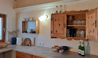 A cozy kitchen with wooden cabinets and dishes. On the countertop, there are a few bottles and a bowl of snacks.