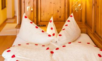 A lovingly decorated bed with heart-shaped pillows. Red rose petals add a special touch to the romantic atmosphere.