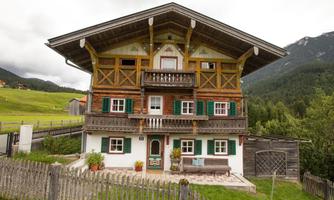 A traditional Alpine wooden house with balconies and colorful shutters. Surrounded by green meadows and mountains.