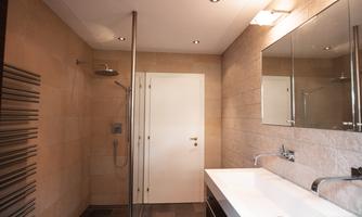 A modern bathroom with a shower and a large mirror. The walls are bright and there are elegant fixtures.