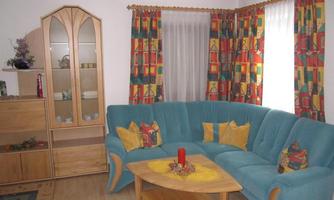 A cozy living room with a blue sofa and colorful curtains. On the table, there is a yellow tablecloth and a decoration.