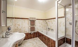 A modern bathroom with a bathtub and a shower. The walls are designed with light tiles and dark accents.