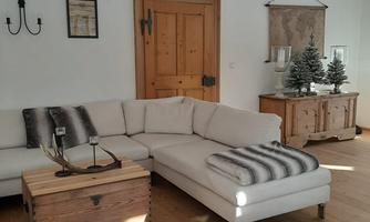 A cozy living room with a large, bright sofa and a wooden table. The space has a warm, inviting character with simple furniture and decorations.