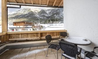 A cozy balcony with a table and chairs. In the background, snow-covered mountains and a winter landscape can be seen.