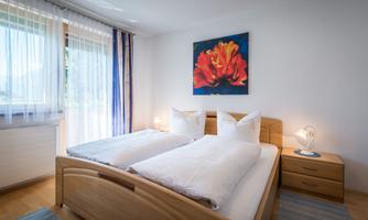 A bright bedroom with a double bed and two white pillows. A colorful flower painting hangs on the wall.