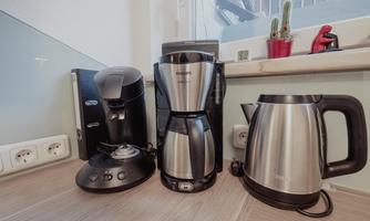 A modern kitchen corner with a coffee machine, a drip coffee maker, and a kettle. The appliances are in glossy black and stainless steel.