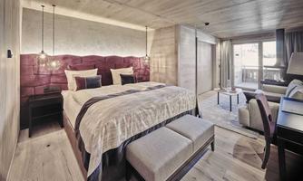 A modern hotel room with a large bed and elegant furnishings. Large windows offer a view of a bright environment.