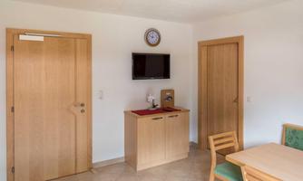 A cozy room with wooden details and a small table. A TV and a clock hang on the wall.
