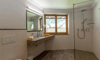 A modern bathroom with a large mirror and a shower. Large windows let in plenty of daylight.