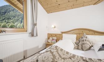 A cozy bedroom with a wooden ceiling and a large window that offers a view of the mountains. The bed is elegantly adorned with decorative pillows and bedding.