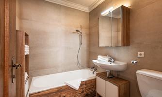 A modern bathroom with a bathtub and a shower. The walls are in neutral tones, and there are wooden and sanitary furnishings.