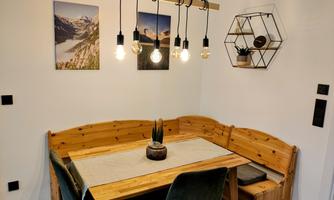 A cozy dining area with a wooden corner and modern lamps. Two pictures and a decorative shelf hang on the wall.