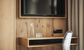 A modern room with a wooden panel and a wall-mounted TV. A small table with a chair and a water carafe is next to it.