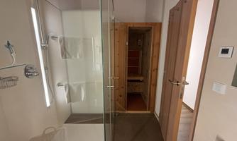 A modern bathroom with a glass shower and bright walls. In the background, a sauna can be seen.