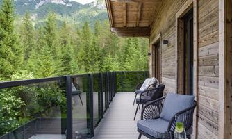 A cozy balcony with two chairs and a table. In the background, green trees and mountains can be seen.