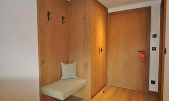An entrance area with wooden walls and a seating area. Several coat hooks hang on the wall.