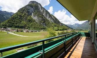 A terrace overlooking an impressive mountain and a green meadow. The sky is clear with a few clouds.