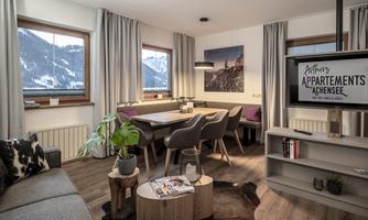 A cozy living space with modern furniture and large windows offering a view of the mountains. The room is bright and inviting, perfect for relaxing moments.