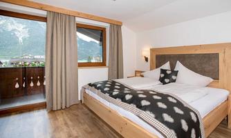A cozy bedroom with a large bed and a modern wooden frame. A beautiful mountain landscape is visible through the window.